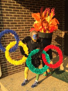 a person in costume standing next to a brick wall and holding a sign with the olympic symbol on it