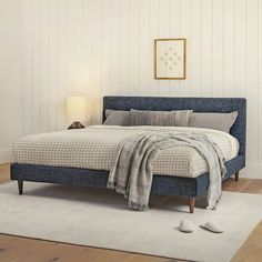 a bedroom with a blue bed and white rugs on the wooden floor, along with two lamps