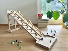 a wooden play set with marbles and a slide in front of a potted plant