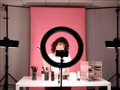 a woman is taking a photo in front of a pink background with her camera and makeup brushes