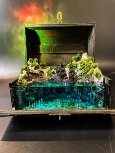 an open box filled with water and rocks on top of a black table next to a wall