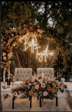 a table topped with flowers and candles under a neon sign that says better together on it