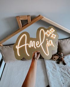 a person holding up a neon sign that says amelja in front of a bed