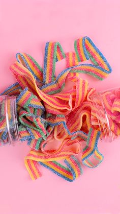 there are many different colored ribbons in the jar on the pink surface, and one is empty