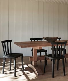 a wooden table with four chairs and a bowl on top of it in front of a white wall