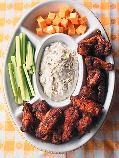 a white plate topped with chicken wings, celery and carrots next to dip