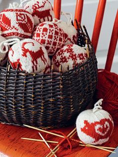 red and white knitted ornaments in a basket on a wooden table next to knitting needles