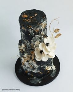 a black and gold wedding cake with white flowers on the top, sitting on a plate