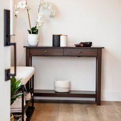 a wooden table with two white vases on top of it next to a plant