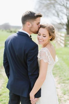 a bride and groom pose for their wedding photo in front of a fenced field