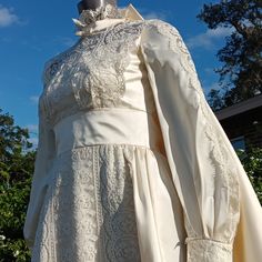 a white dress on display in front of some trees and blue sky with clouds behind it