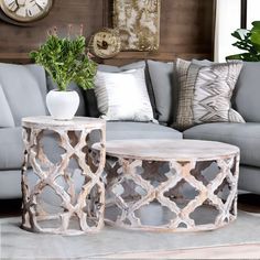 two tables sitting on top of a rug in front of a gray couch with pillows