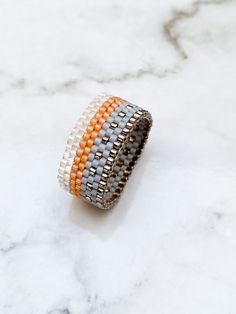 an orange, grey and white beaded bracelet on a marble surface with text overlay