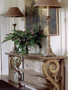 a table with two lamps and a potted plant sitting on it in front of a painting