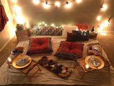 a table topped with lots of food next to a bed covered in lights and blankets