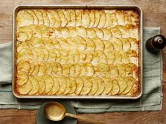 a baking dish filled with potatoes on top of a wooden table next to a spoon