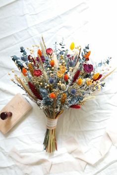 a bouquet of dried flowers sitting on top of a white sheet covered floor next to a piece of wood