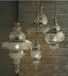 an assortment of hanging lights made out of silver filigrees on a wooden wall