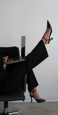 a woman sitting in a chair with her legs crossed and holding a laptop on her lap