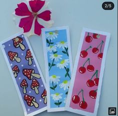 three bookmarks with cherries, daisies and mushrooms on them next to a flower