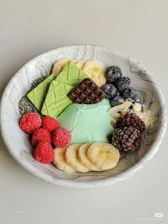 a bowl filled with assorted fruit and chocolates on top of a white table