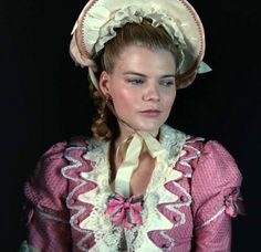 a woman in a pink dress and hat with braids on her head is looking at the camera