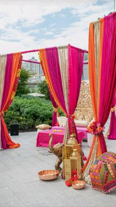 an outdoor wedding setup with pink and orange draping, gold decorations and candles