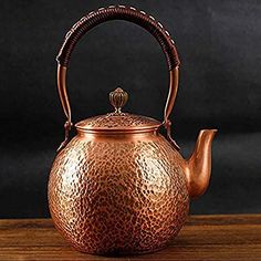 a copper tea pot with a handle on a wooden table