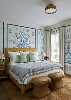 a bedroom with blue and white wallpaper, a large bed and two stools