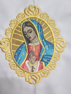 the embroidered image of mary is shown in gold and blue on a white shirt with an ornate border