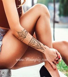 a woman sitting on the ground with her legs crossed and tattoos on her arm,