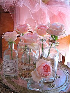 pink roses are in glass vases on a tray with an empty bottle and two bottles