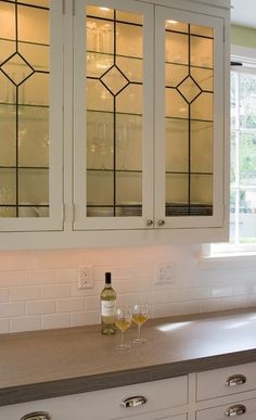 two wine glasses are sitting on the counter in front of some cupboards with glass doors