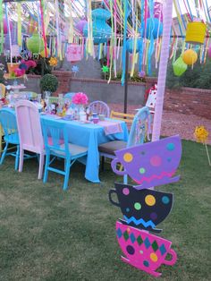 an outdoor party setting with colorful decorations and tables set up in the grass for a tea party