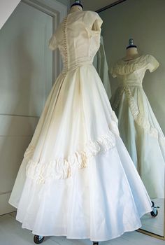 two dresses are on display in front of a mirror, one is white and the other is ivory