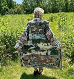 a woman is standing in the grass with her back to the camera and she's wearing a jacket that has boats on it