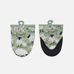 a pair of oven mitts with sheeps on green and black fabric, hanging from the side