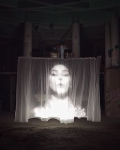 a woman's face is projected through curtains in the middle of a dark room