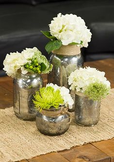 three vases with flowers are sitting on a table top near a black leather couch