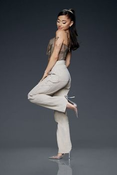 a woman is standing on one leg with her hands in the air while wearing white pants and heels