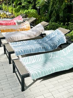 four lounge chairs are lined up next to each other on a brick patio with palm trees in the background