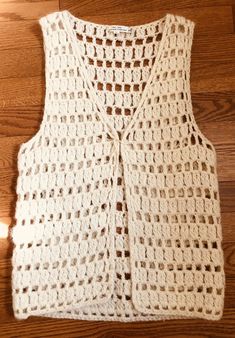 a white crocheted vest sitting on top of a wooden floor