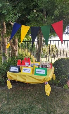 a yellow table topped with lots of cake and desserts next to a fenced in area