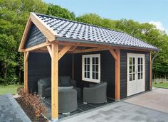 a black shed with two chairs and a couch in the yard next to some trees