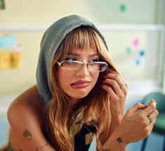 a woman wearing glasses and a hoodie is holding her hand up to her ear