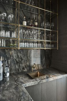 a kitchen with marble counter tops and shelves filled with wine glasses, liquor bottles, and other glassware