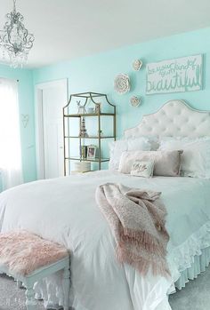 a white bed sitting in a bedroom next to a chandelier and pillows on top of it