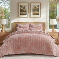 a bed with pink bedspread and two pictures on the wall in front of it