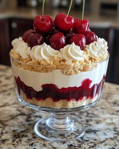 a dessert with cherries and whipped cream in a glass dish on a granite countertop