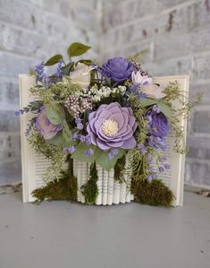 a bouquet of flowers sitting on top of an open book with moss growing out of it